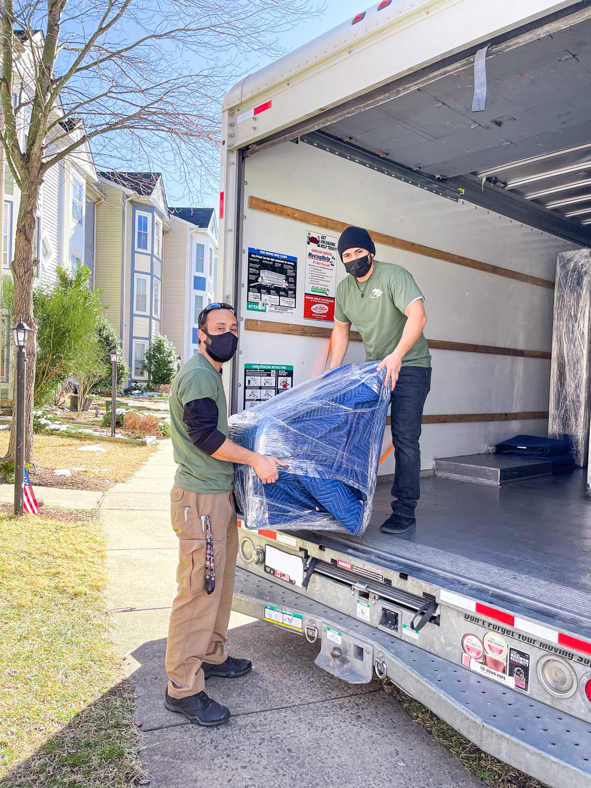 Movers carrying wrapped furniture outside an apartment building