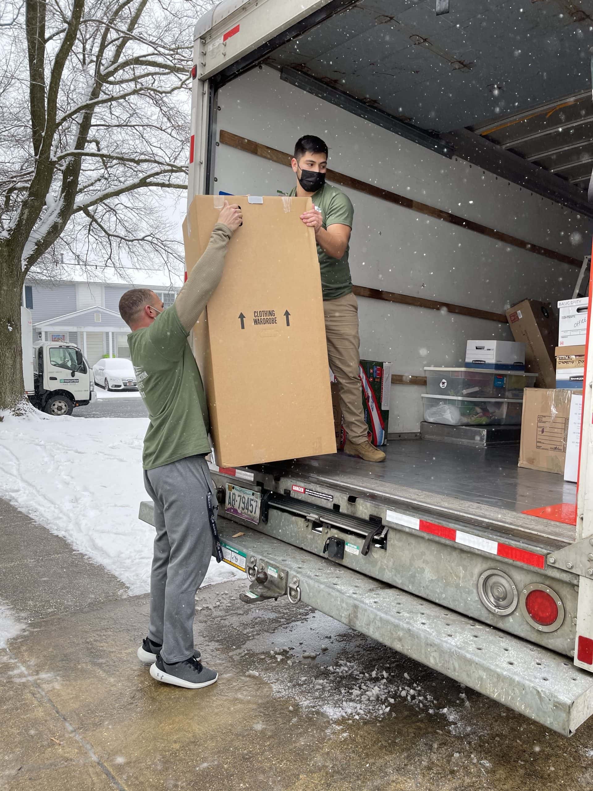 Movers loading wrapped furniture into the back of a moving truck